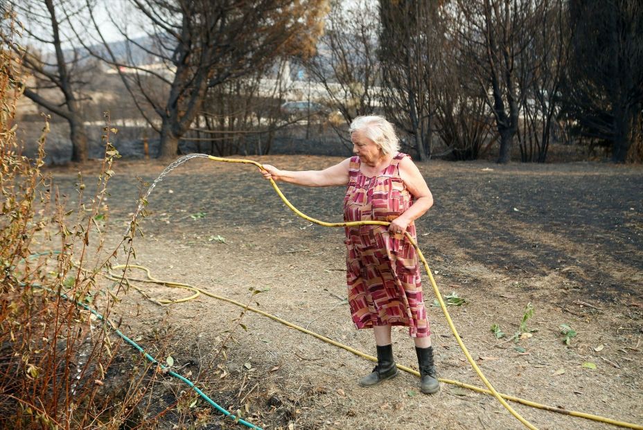Una mujer refresca el terreno para que no se reproduzca el fuego, a 21 de agosto de 2025, en A Gudiña, Ourense, Galicia