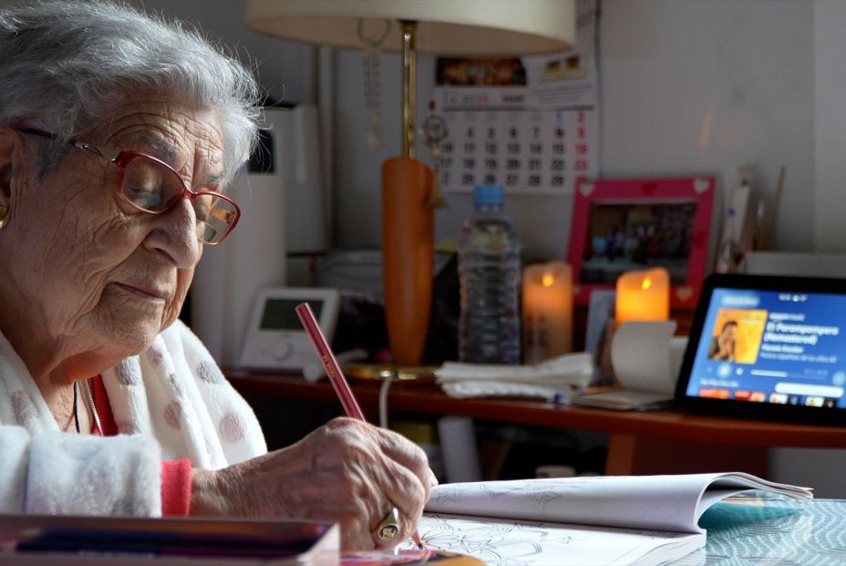 Una mujer mayor hace tareas de escritura, junto al dispositivo de voz de Cruz Roja. Fuente: Europa Press.