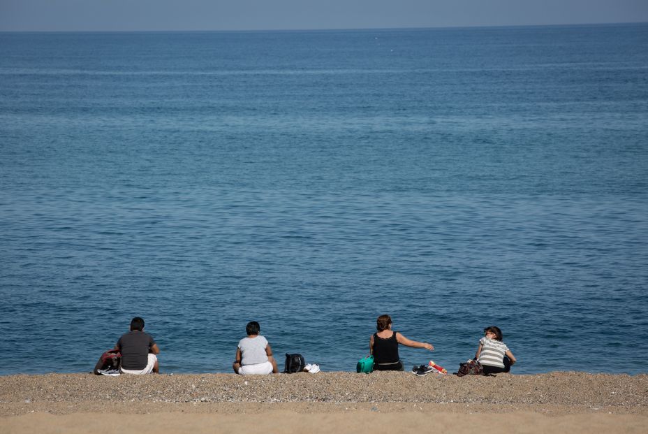 varias personas sentadas playa barceloneta respetan distancia seguridad dia