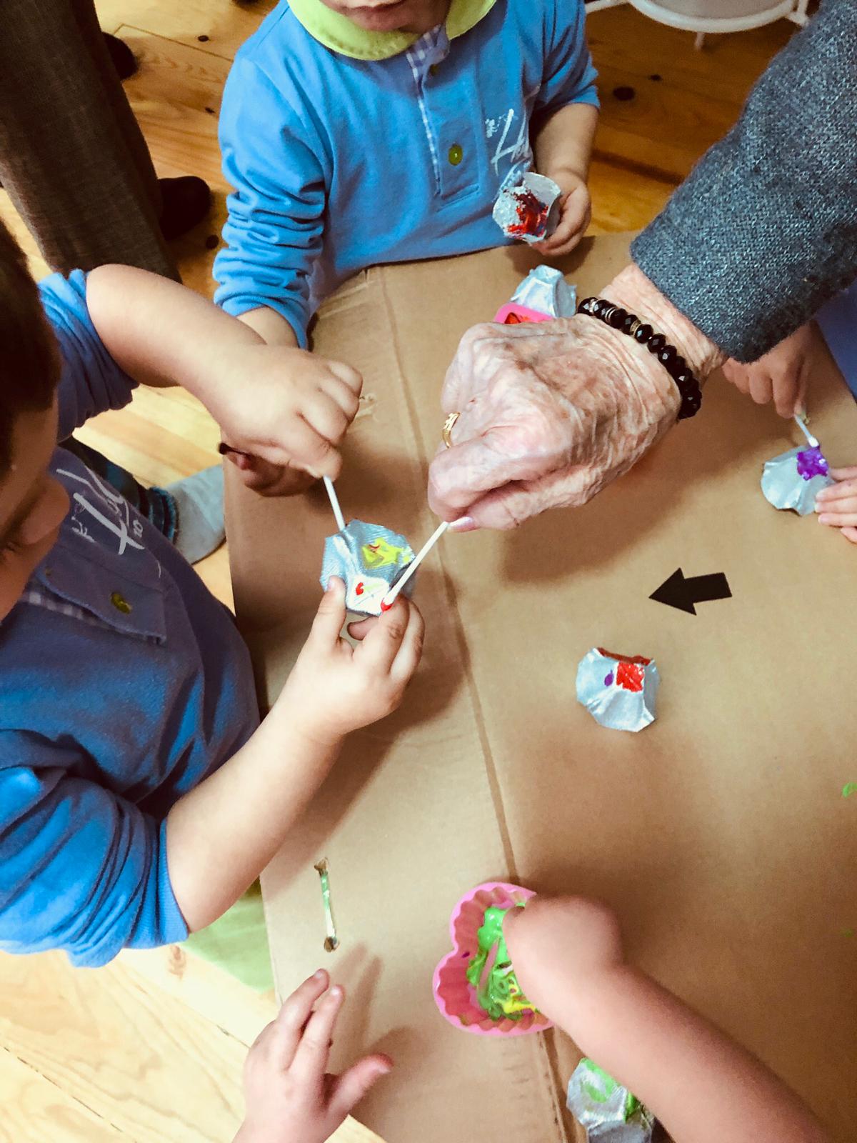 Niños y mayores haciendo manualidades en la guardería Hadas y Duendes.