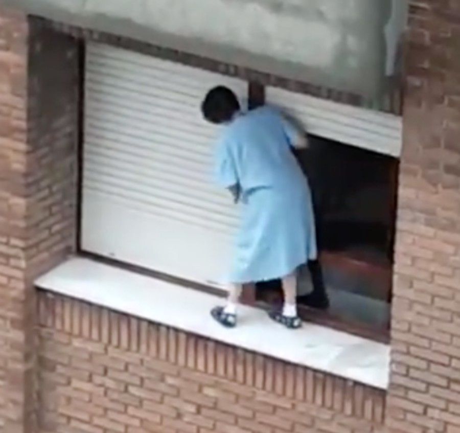 Acto temerario: una mujer sale al alféizar de su ventana para limpiar la persiana