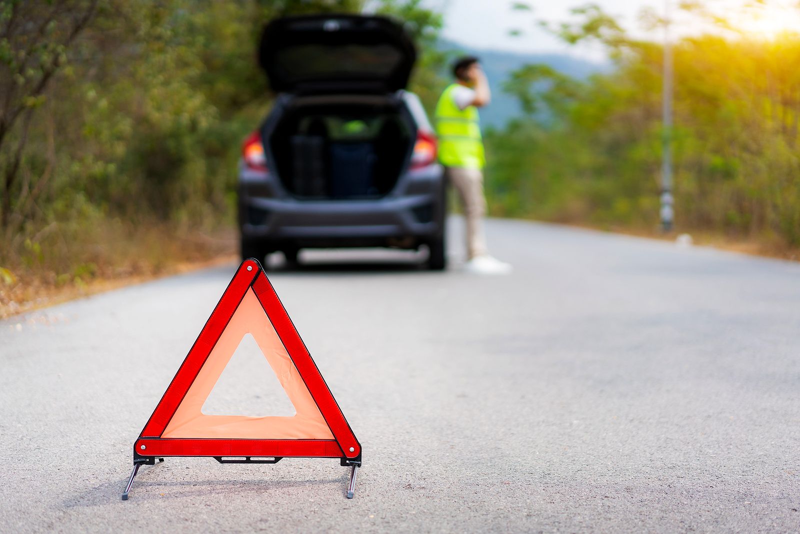 Conductor con vehículo inmovilizado y triángulo colocado en la vía.