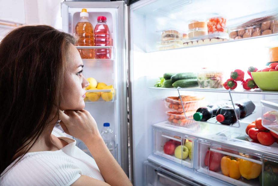 Mujer mirando nevera ordenada y asegurándose de la temperatura de seguridad de los alimentos (bigstock)