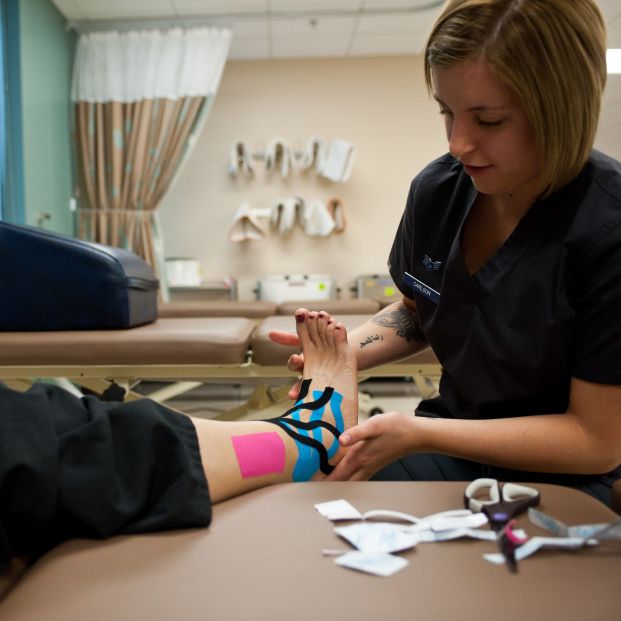 Fisio pegando kinesiotaping en el tobillo a un paciente (Creative commons)