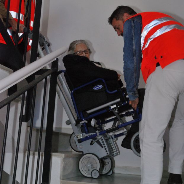 Dos trabajadores de la Cruz Roja ayudan a bajar a una persona mayor con una 'Scalamóbil'.