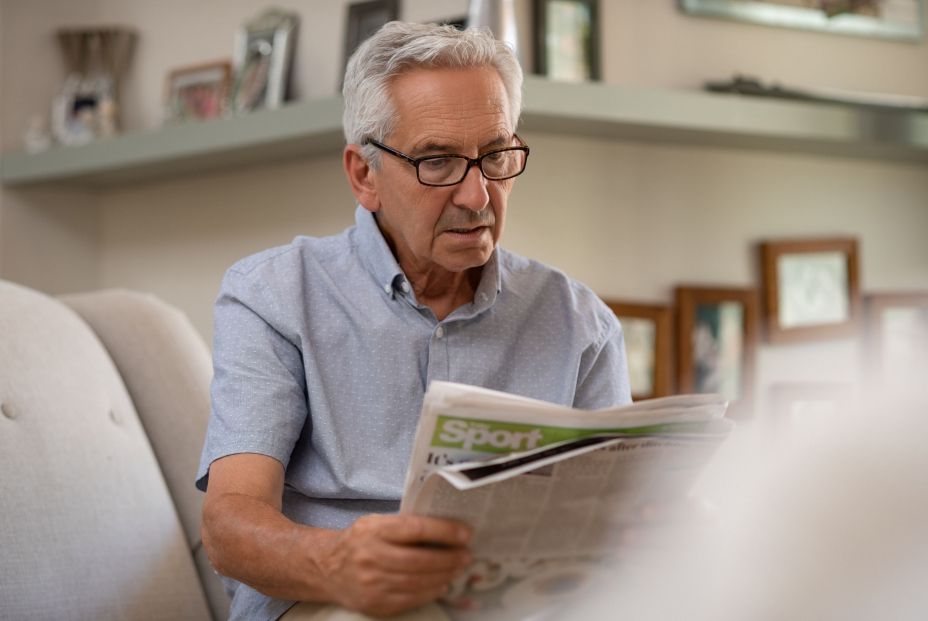Persona adulta con gafas leyendo periódico a la distancia correcta