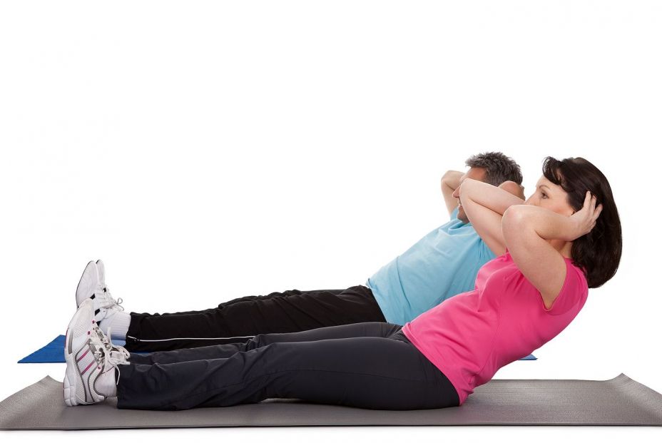 Mujer y hombre realizando abdominales con las manos en la nuca. Foto: Bigstock 